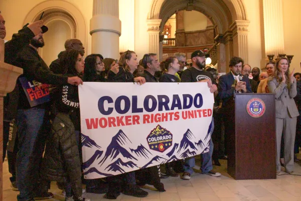 A crow of workers stands holding a banner that say "Colroado Workers Rights United" with a blue mountain range graphic underneath